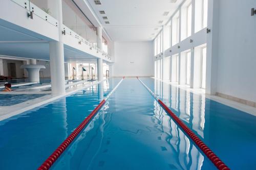 a large indoor swimming pool with blue water at Aqvatonic Hotel - Steaua de Mare in Eforie Nord