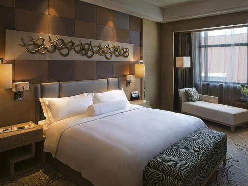 a hotel room with a large white bed and a chair at Movenpick Hotel Enshi in Enshi