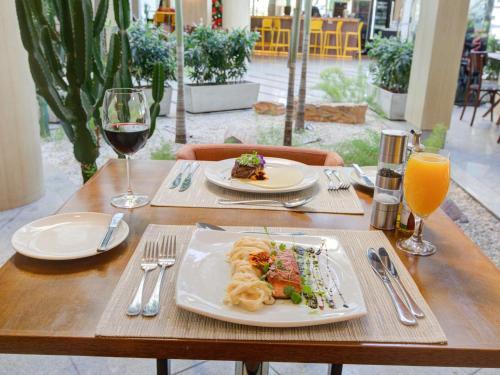 a table with two plates of food and a glass of wine at Mercure Rio de Janeiro Barra da Tijuca in Rio de Janeiro
