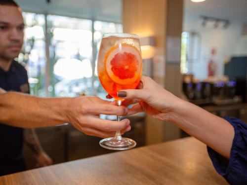 a person holding a glass with a fruit in it at Mercure Rio de Janeiro Barra da Tijuca in Rio de Janeiro
