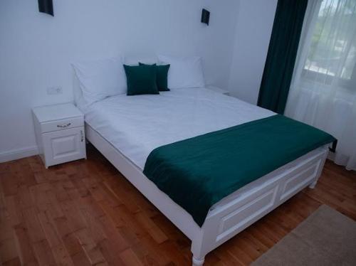 a white bed with a green blanket and a night stand at Pensiunea Graniti in Lunca