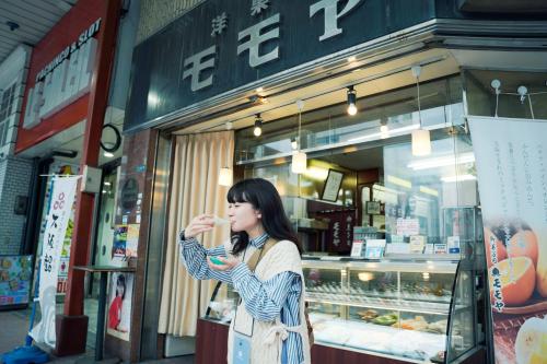 a woman eating food in front of a store at SEKAI HOTEL Deep Osaka Experience in Osaka