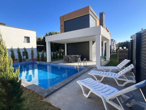 a swimming pool with two lounge chairs and a house at Oa Ceșme Villa in Cesme