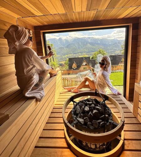 two women sitting on the porch of a sauna with a fire pit at Osada Gubałówka na Polanie Pająkówka & SPA in Kościelisko