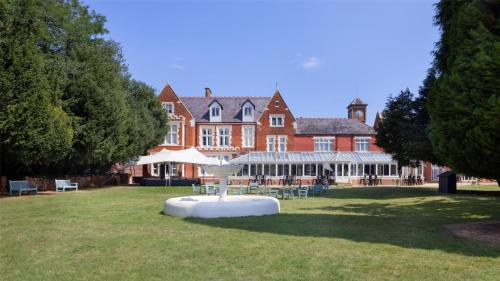 a large building with a table and chairs in the grass at DoubleTree by Hilton St. Anne's Manor in Bracknell