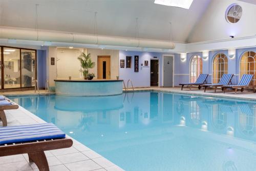 a large swimming pool with blue chairs in a building at DoubleTree by Hilton St. Anne's Manor in Bracknell