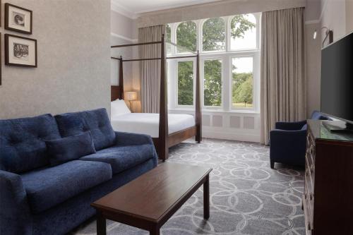 a living room with a blue couch and a bed at DoubleTree by Hilton St. Anne's Manor in Bracknell
