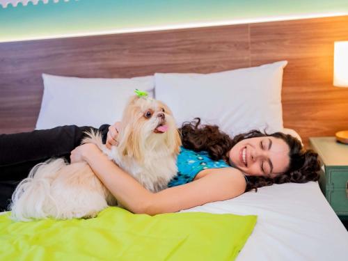 a woman laying on a bed with a dog at ibis Styles Sorocaba Santa Rosalia in Sorocaba