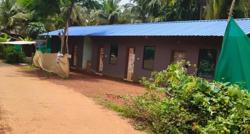 a small building with a blue roof next to a dirt road at Nature Nest Rooms in Gokarna