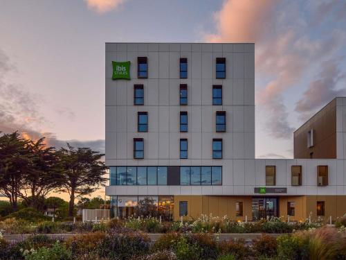 a tall white building with a green sign on it at Ibis Styles Montpellier Aéroport Parc Des Expos in Mauguio