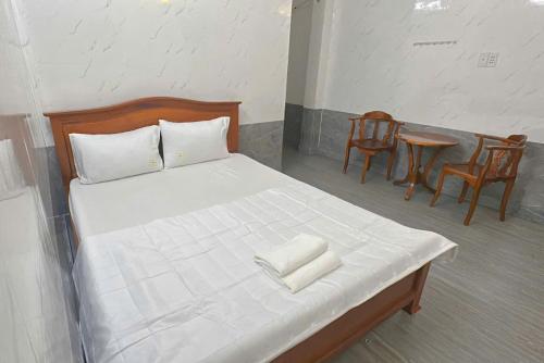a bedroom with a bed with white sheets and chairs at Nhà Nghỉ Quỳnh Thoa in My Tho