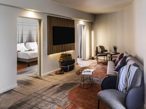 a living room with a couch and a tv and a bed at Novotel Cambridge North in Cambridge
