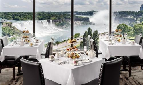 a restaurant with white tables and chairs and a view of niagara falls at The Brock Niagara Falls Fallsview, Tapestry by Hilton in Niagara Falls