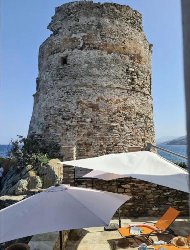 an umbrella and chairs in front of a tower at Casa Torra d'Erbalunga in Brando