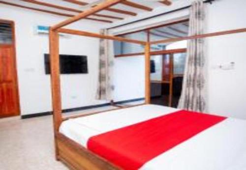 a bedroom with a canopy bed with a red blanket at Utulivu Bungalow in Nungwi