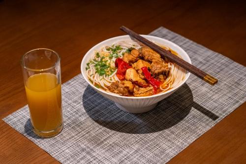 a bowl of noodles and a glass of orange juice at YiQuan RIVERVIEW B&B in Fenghuang