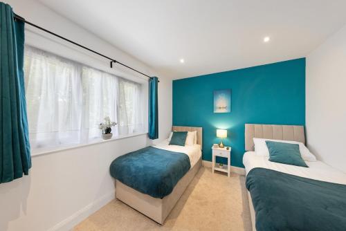 Luxury 4BR Home with Hot Tub, Sleep 8, Free Parking, Garden في Kenley: سريرين في غرفة بجدران زرقاء