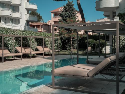 a pool with chairs and an umbrella next to a building at Prinsotel La Pineda in Cala Ratjada