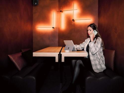 a woman talking on a phone at a table with a laptop at Tribe Carcassonne in Carcassonne