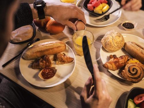a table with plates of food and a person holding a knife at ibis Styles Arnhem Centre in Arnhem