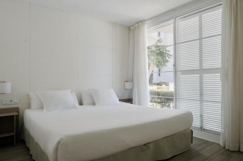 a white bedroom with a large bed and a window at Prinsotel La Pineda in Cala Ratjada