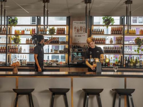 two people standing at a counter in a bar at Ibis Paris Gare Montparnasse Catalogne in Paris