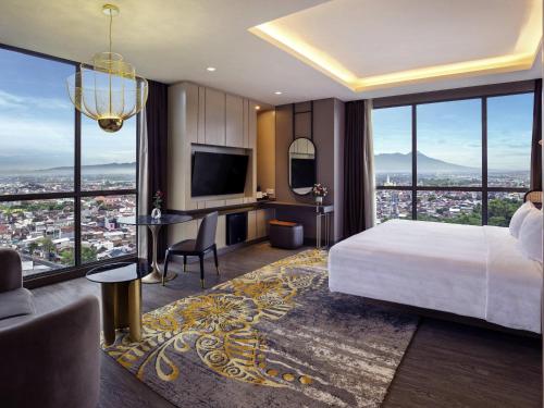 a bedroom with a bed and a desk and a television at Grand Mercure Malang in Malang