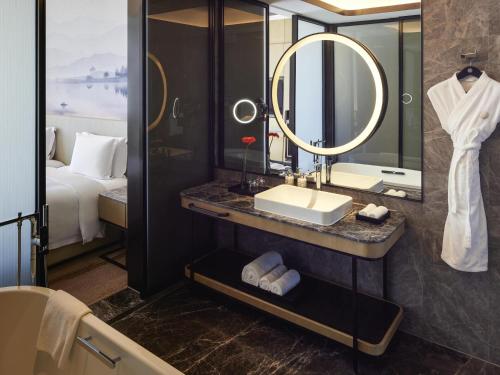 a bathroom with a sink and a mirror and a bed at Pullman Suzhou Taicang in Taicang