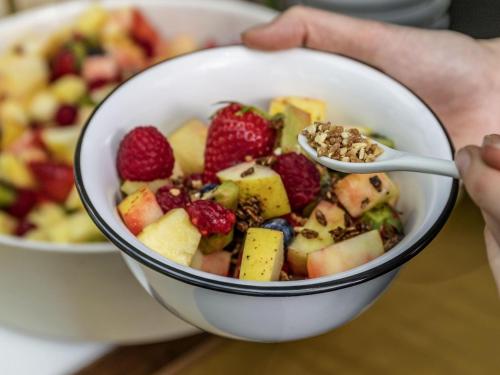 a person holding a bowl of fruit with a spoon at Novotel Lencois Paulista in Lençóis Paulista