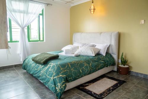 a bedroom with a bed with a green blanket and white pillows at VillaromAfrica Staycations-Gold Suite in Eldoret