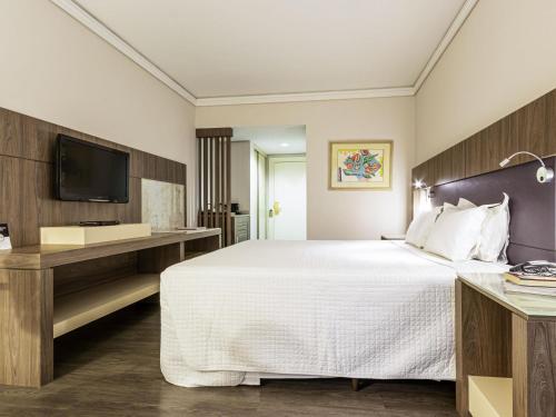 a hotel room with a bed and a tv at Grand Mercure Curitiba Rayon in Curitiba
