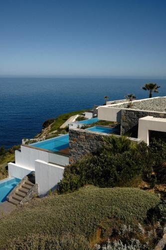 a house on a hill with the ocean in the background at Rock Bay Villas - Luxury Villas in Crete in Agia Pelagia