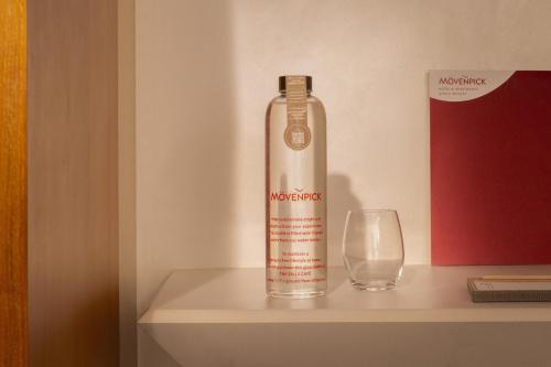 a bottle of alcohol sitting on a shelf next to a glass at Mövenpick Hotel & Apartments Ghala Muscat in Muscat