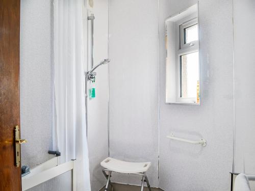 a white bathroom with a shower and a chair at Woodend Farmhouse Halmyre in Haugh of Urr