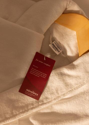 a red tag sitting on top of a bed at Mövenpick Hotel & Apartments Ghala Muscat in Muscat