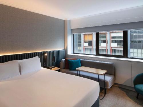a hotel room with a bed and a chair and window at Novotel Sydney City Centre in Sydney