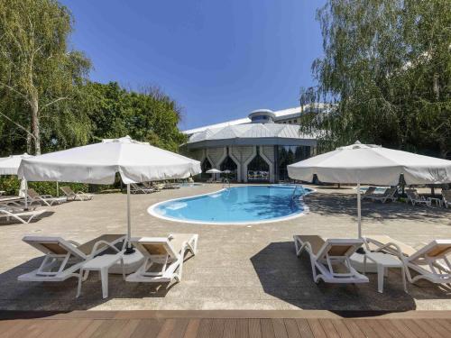 a pool with chairs and umbrellas next to a building at Swissôtel Wellness Resort Alatau Almaty in Almaty