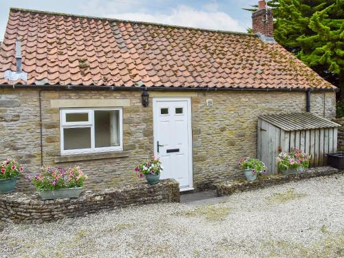 a small stone cottage with a white door and flowers at Blacksmiths Cottage in Gillamoor