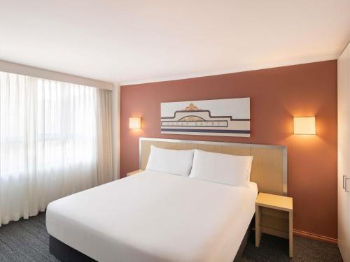 a hotel room with a large white bed and a window at Mercure Newcastle in Newcastle