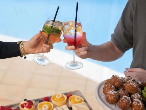 two people holding cocktails in front of a table with food at Mercure Newcastle in Newcastle