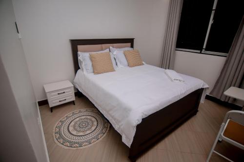 a small bedroom with a bed with white sheets and pillows at Reza stays apartment -Makumbusho behind Mwanga Tower in Dar es Salaam