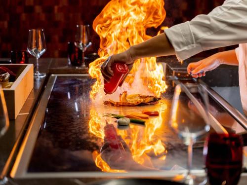 a person cooking food on a grill in flames at Club Privé By Rixos Saadiyat in Abu Dhabi