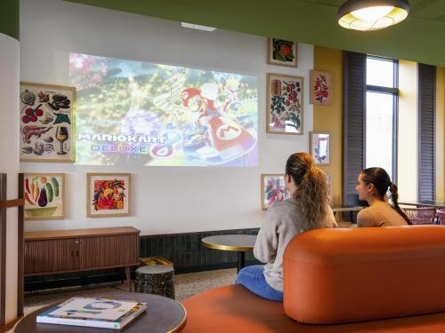 two women sitting in a waiting room watching a presentation at ibis Styles Versailles Saint Quentin en Yvelines in Saint-Cyr-lʼÉcole