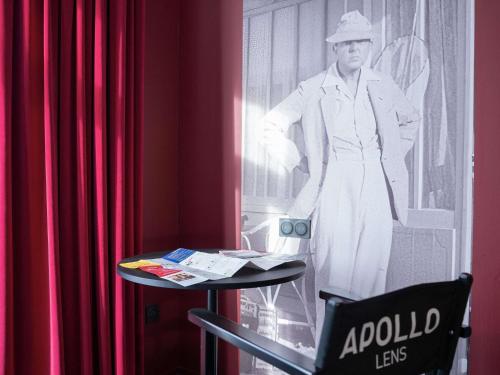 a black and white photo of a woman standing next to a table at ibis Styles Lens Centre Gare in Lens