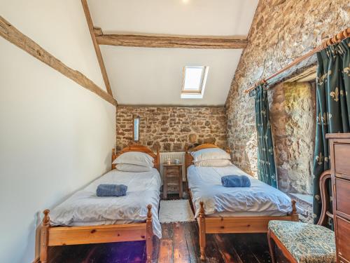 two beds in a room with a stone wall at Haytongate Barn in Walton