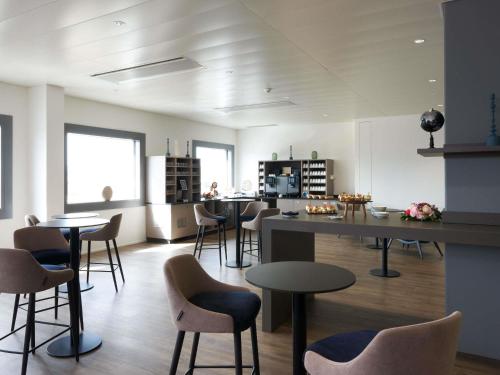a room with chairs and tables and a kitchen at Mercure Geneva Airport in Geneva