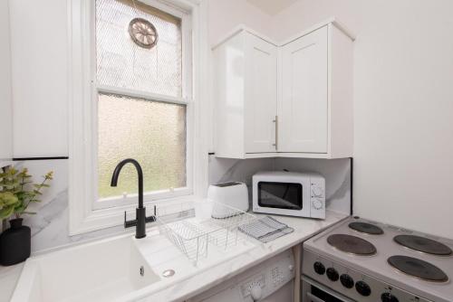 a white kitchen with a sink and a microwave at Northcote apartment in Hawick