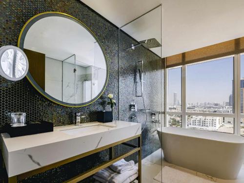 a bathroom with a tub and a sink and a mirror at Movenpick Jumeirah Village Triangle in Dubai