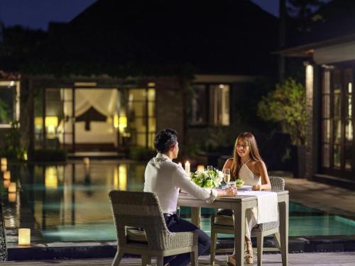 a man and woman sitting at a table by a pool at Peppers Seminyak in Seminyak