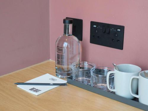 a bottle of alcohol sitting on a table with cups at TRIBE London Canary Wharf in London